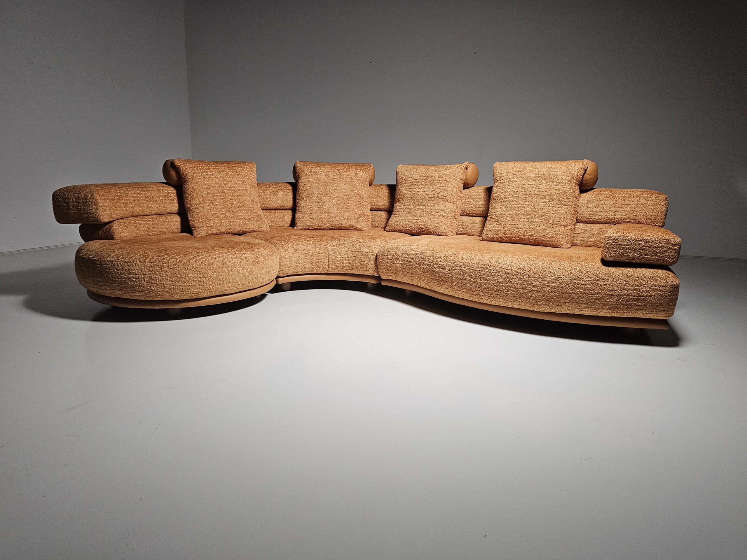 Curved orange modular sofa with matching square cushions in a minimalist studio setting.